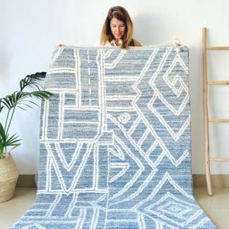 Woman holding a handmade, Moroccan rug with white line designs on a mixed blue background.