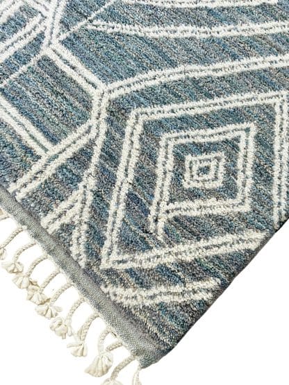 Close up of a handmade, Moroccan rug with white line designs on a mixed blue background.