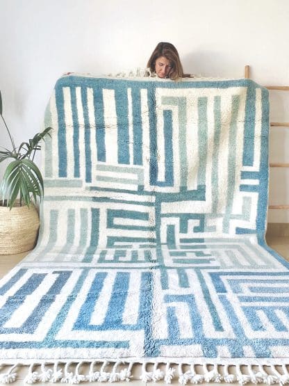 Woman holding a Beni Ourain Moroccan Rug with a blue and white maze design.