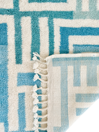 Close up of the folded over corner of a Beni Ourain Moroccan Rug with a blue and white maze design.