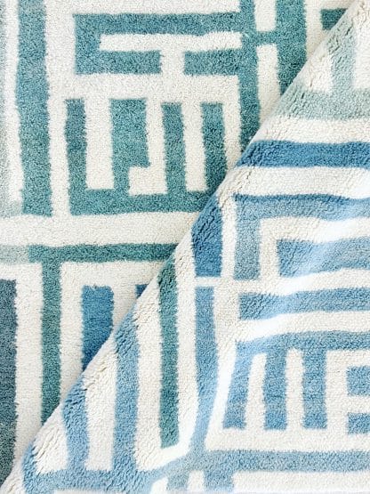 Close up of a Beni Ourain Moroccan Rug with a blue and white maze design and a diagonal fold.