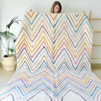 Woman holding a Beni Ourain Moroccan rug with multicoloured zigzags.