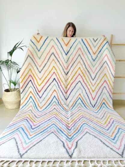 Woman holding a Beni Ourain Moroccan rug with multicoloured zigzags.