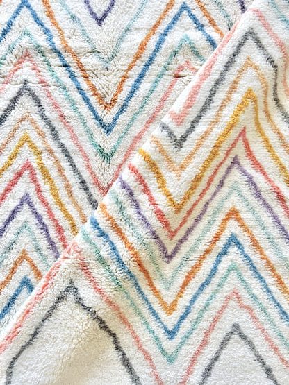 Close up of a a Beni Ourain Moroccan rug with multicoloured zigzags. There is a diagonal fold in the rug.