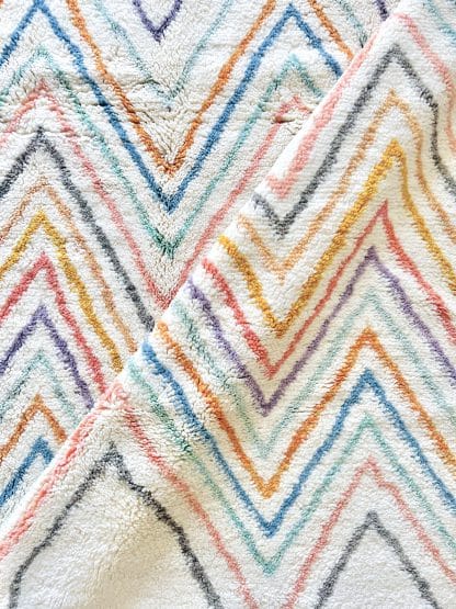 Close up of a a Beni Ourain Moroccan rug with multicoloured zigzags. There is a diagonal fold in the rug.