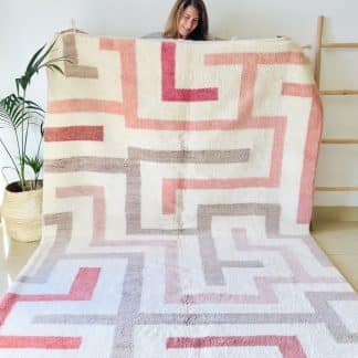 Woman holding a Beni Ourain Moroccan Rug - with a bold cream, beige and pink maze design.