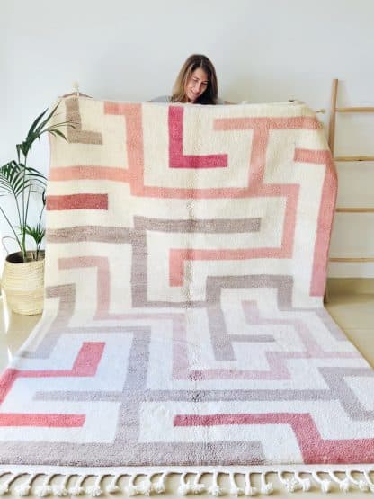 Woman holding a Beni Ourain Moroccan Rug - with a bold cream, beige and pink maze design.