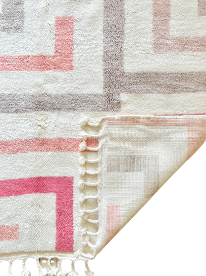 Close up of the folded corner of a Beni Ourain Moroccan Rug with a bold cream, beige and pink maze design.