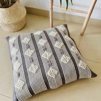 Moroccan floor pillow made with dark grey and off-white wool on a marble floor.