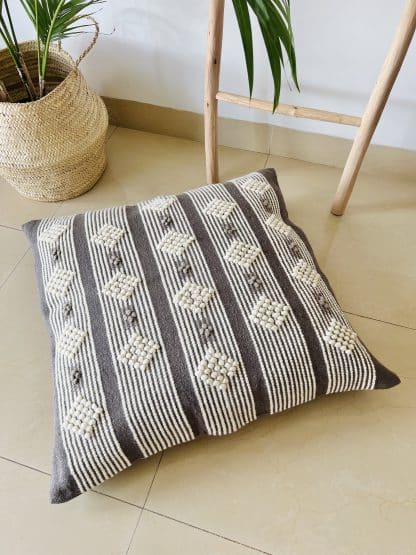 Moroccan floor pillow made with dark grey and off-white wool on a marble floor.