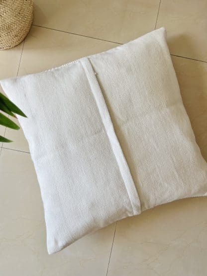 Upside down Moroccan floor pillow made of off-white wool with little woollen balls arranged in geometric designs on a marble floor. There is a plant in the shot.