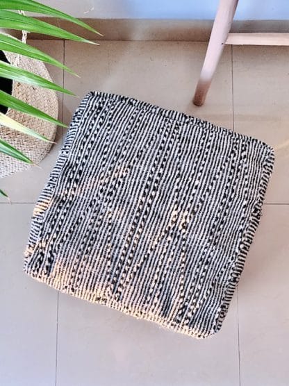 Aerial shot of a Black and white Moroccan floor pouf handmade from a traditional zanafi kilim with raised designs on a marble floor with a plant and wooden ladder.