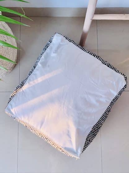 Aerial shot of an upside down Black and white Moroccan floor pouf handmade from a traditional zanafi kilim with raised designs on a marble floor with a plant and wooden ladder.