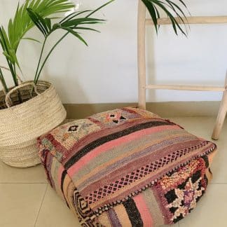 Colourful Moroccan floor pouf handmade from a vintage flat weave kilim with multicoloured Berber designs on a marble floor with a plant and wooden ladder in the background.