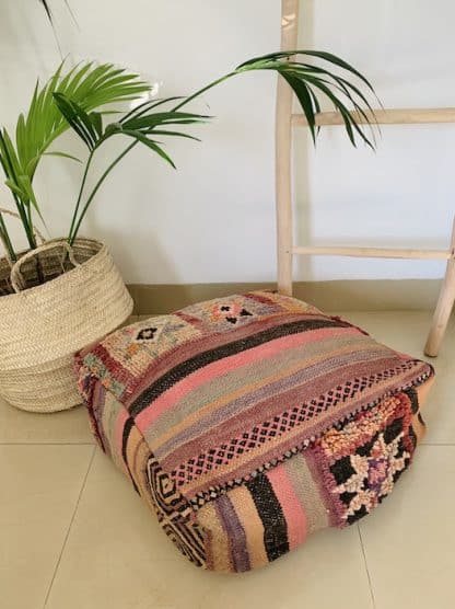 Colourful Moroccan floor pouf handmade from a vintage flat weave kilim with multicoloured Berber designs on a marble floor with a plant and wooden ladder in the background.