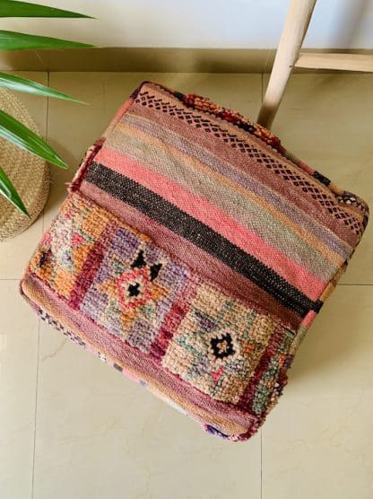 Aerial shot of a colourful Moroccan floor pouf handmade from a vintage flat weave kilim with multicoloured Berber designs on a marble floor with a plant and wooden ladder in the background.