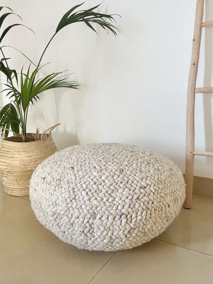 Beige Braided Pouf with a plant and wood ladder in the background.