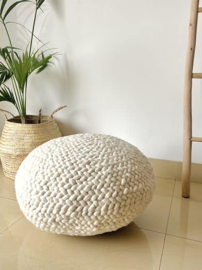 Ivory Braided Pouf with a plant and a wooden ladder in the background