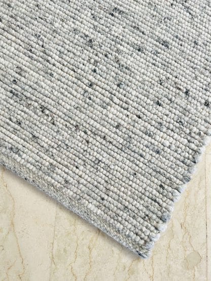 Close up shot of the corner a plush Moroccan rug featuring a flat weaving technique using grey wool felt