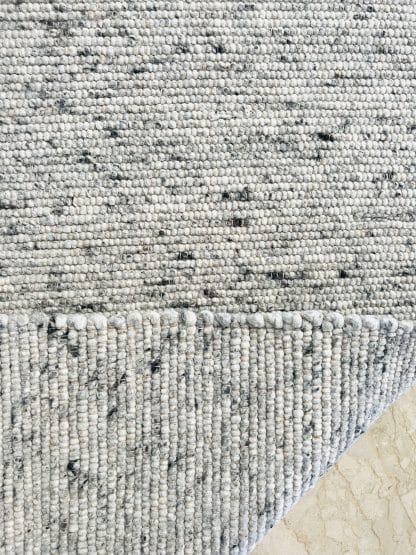 Close up shot of the folded corner a plush Moroccan rug featuring a flat weaving technique using grey wool felt