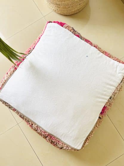 Upside down Moroccan floor pouf handmade from a vintage low pile rug. It features geometric Berber designs in shades of hot pink, charcoal grey and beige. Pictured on a marble floor.