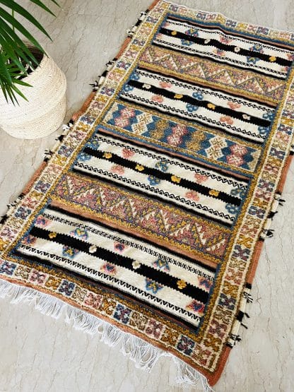 Aerial shot of an off-white, black and orange with tufted designs in shades of pink, blue, and yellow. Pictured on a marble floor with a palm plant.