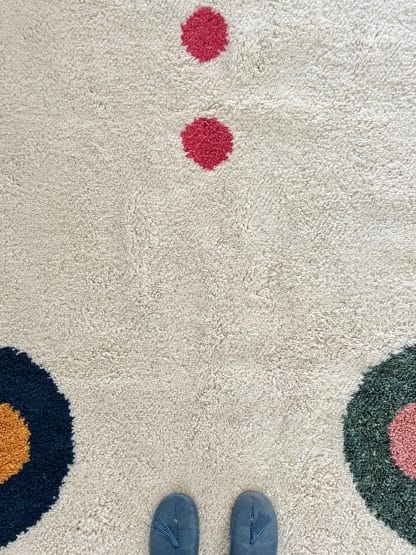 Close up of a Beni Ourain Moroccan Rug created in collaboration with White Otter Design Co. It features a cream base with green and blue petals, and red dots.