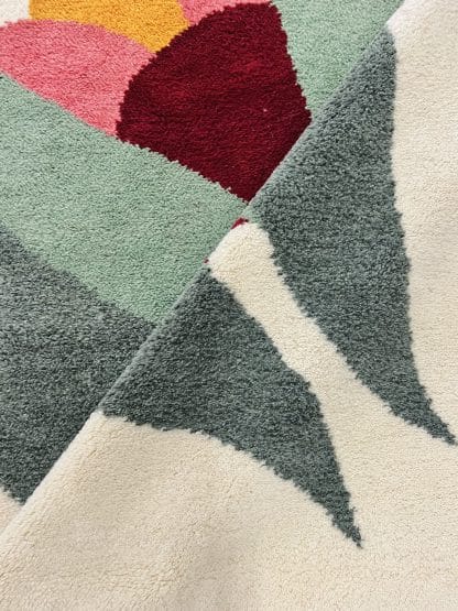 Close up of a fold in a hand-knotted Beni Ourain style rug created with White Otter Design Co. It features a cream base with a large floral design in green, red, pink and yellow.