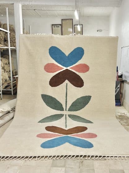 Full of a hand-knotted Beni Ourain style rug created with White Otter Design Co. It features a cream base with a large floral design in green, red, pink and yellow.