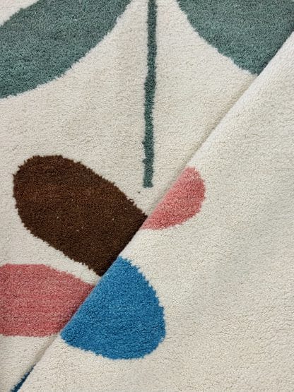 Close up of a fold in a hand-knotted Beni Ourain style rug created with White Otter Design Co. It features a cream base with a large floral design in green, red, pink and yellow.