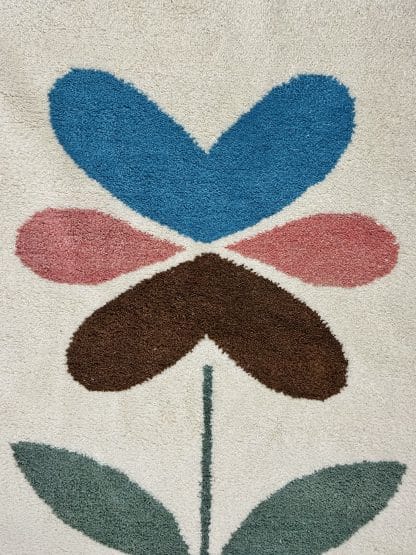 Close up of a hand-knotted Beni Ourain style rug created with White Otter Design Co. It features a cream base with a large floral design in green, red, pink and yellow.