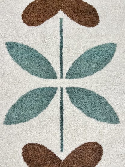 Close up of a hand-knotted Beni Ourain style rug created with White Otter Design Co. It features a cream base with a large floral design in green, red, pink and yellow.